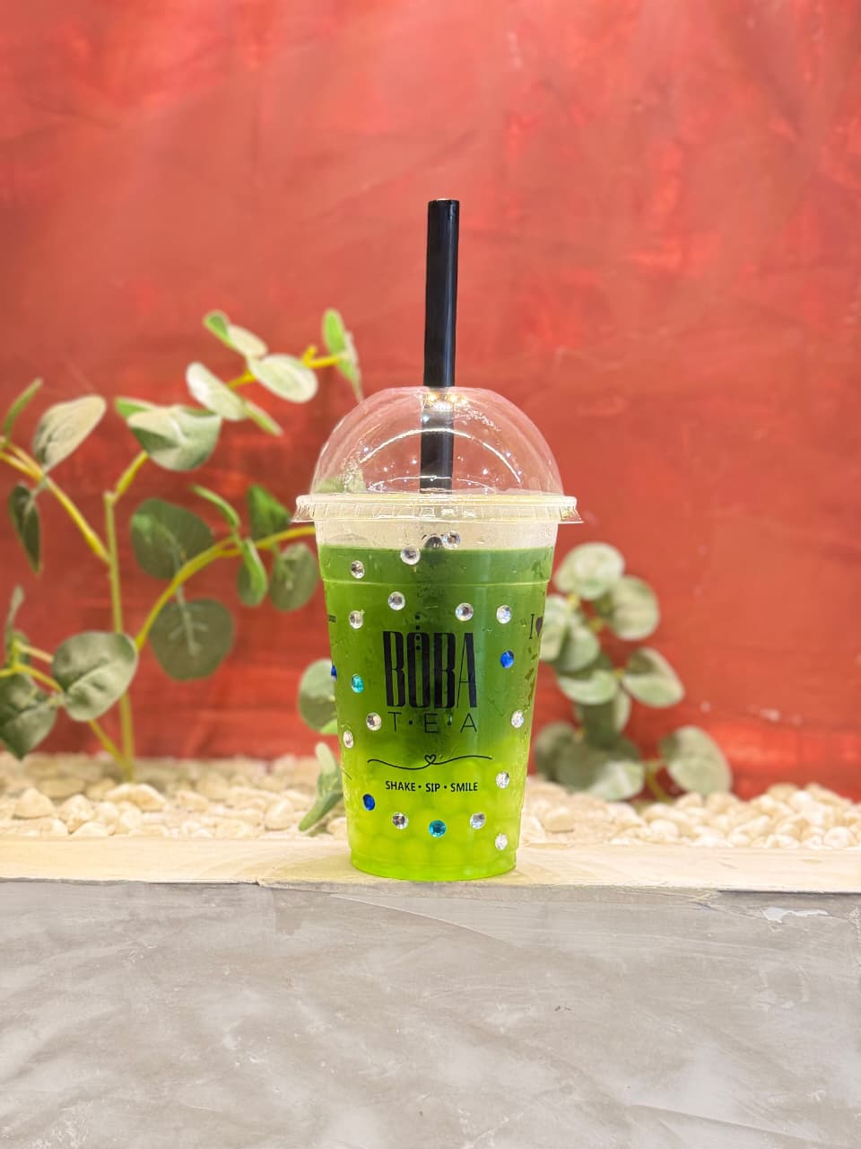 Bebida verde de Bōba Tea frente a un fondo rojo